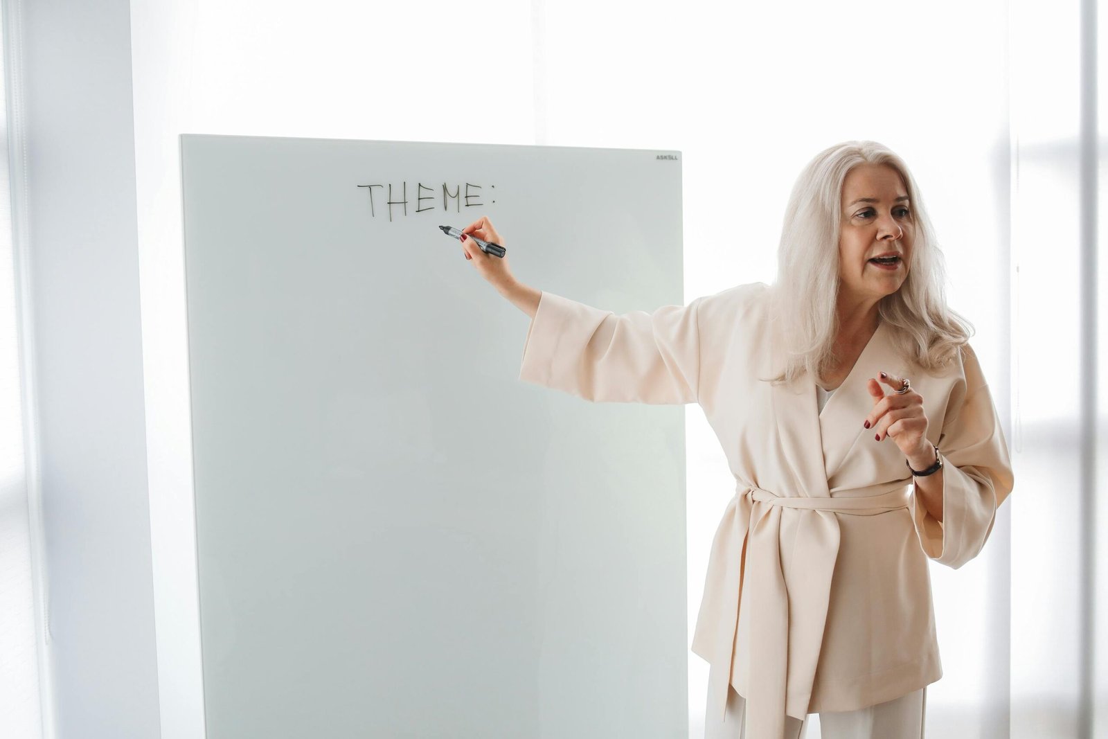 Adult female instructor teaching a theme on a whiteboard in a modern classroom setting.